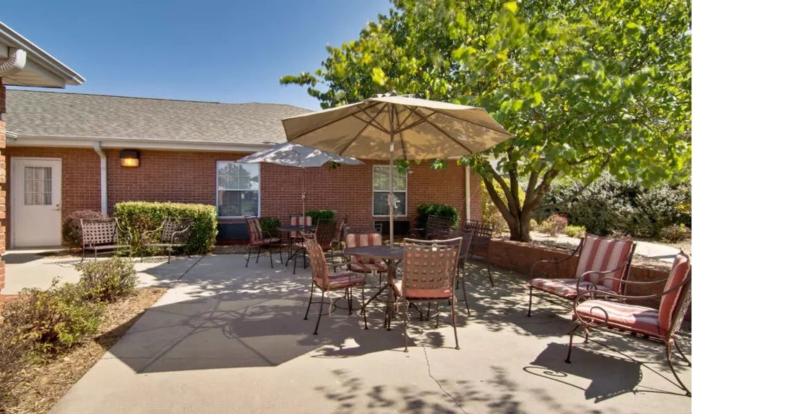 A sunny patio area with outdoor seating and umbrella, surrounded by greenery.