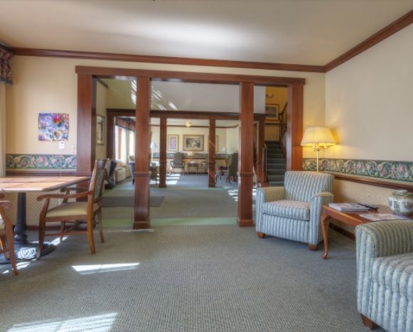 A cozy living room with a carpeted floor, featuring comfortable seating and wooden beams.