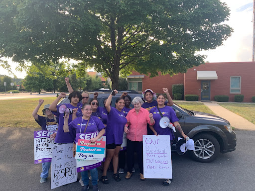 A group of enthusiastic community members, clad in purple, gathers to advocate for workers' rights with signs and cheers.