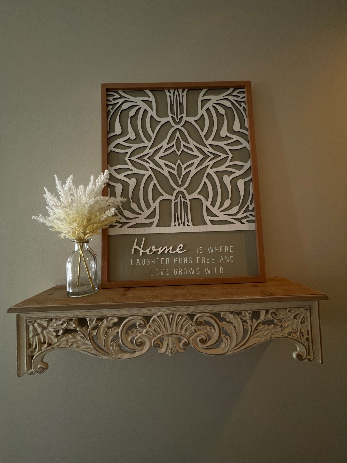 A beautifully arranged wooden shelf featuring intricate wall art and a vase of flowers.