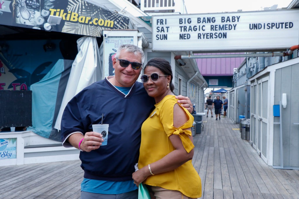 A couple poses happily in front of a marquee sign outdoors.