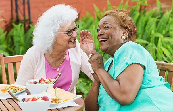 Two elderly women sharing a joyful moment outdoors.