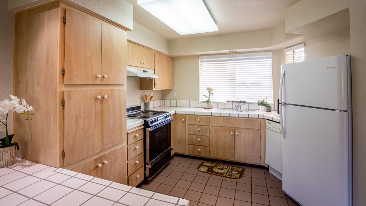 A kitchen with wooden cabinets, a stove and oven, and a tiled floor.