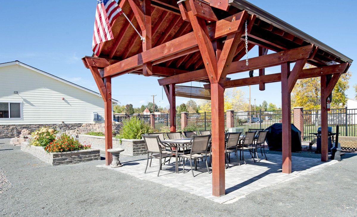 A wooden pergola with a dining area and an American flag, situated on a patio.
