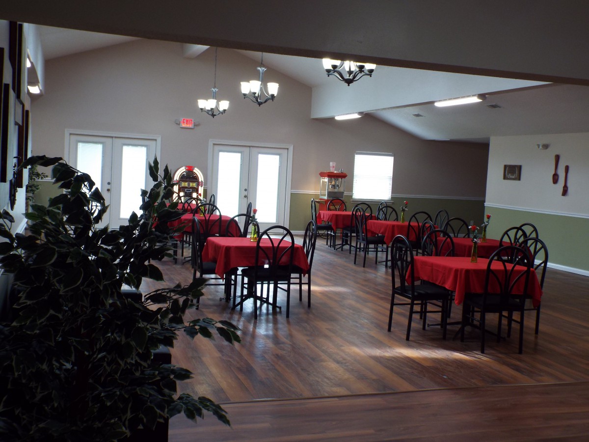 An empty dining room with tables set with red tablecloths and black chairs.