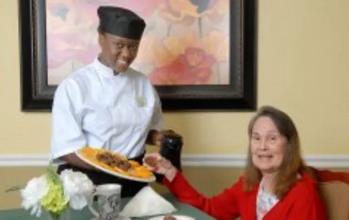 A chef serves food to a smiling customer in a restaurant setting.