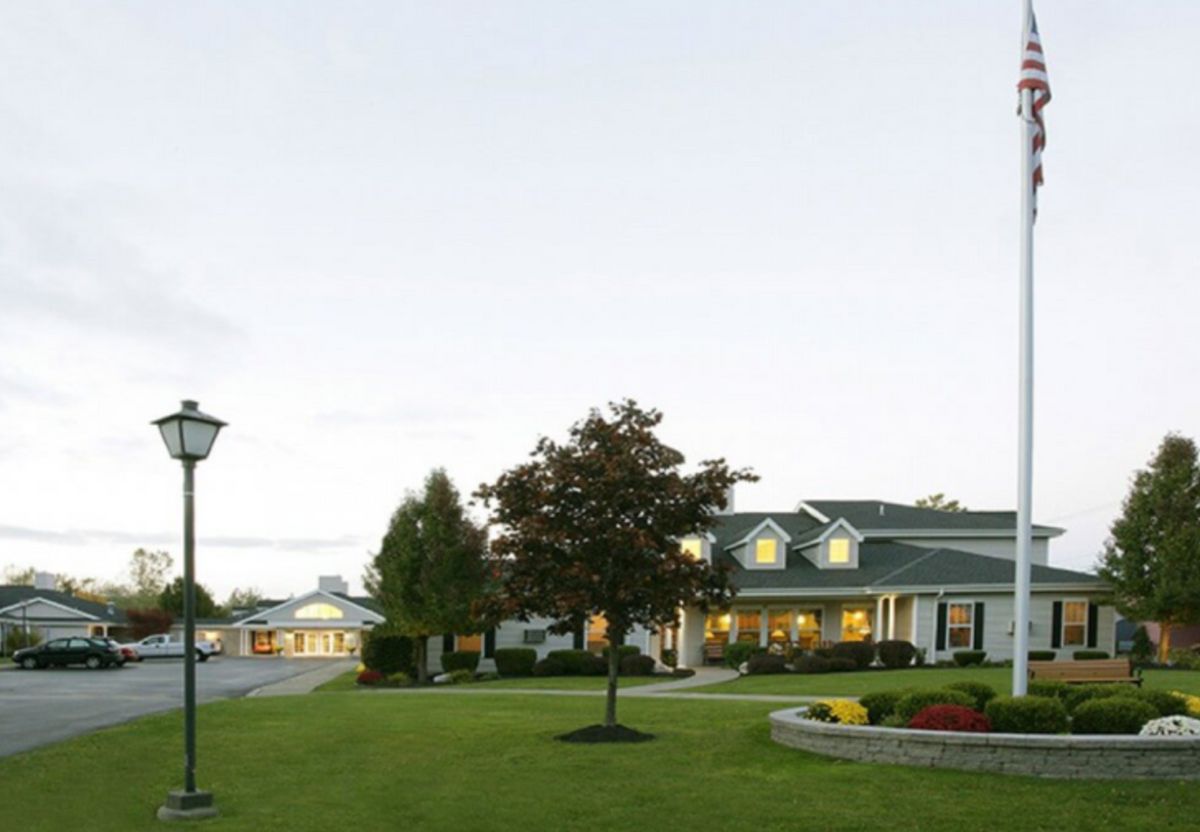 A picturesque landscape with a house, well-maintained lawn, and trees under a clear sky.