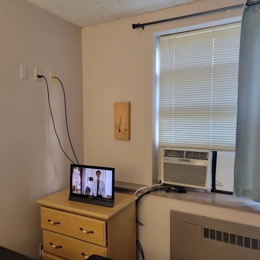 A cozy room featuring a television on a chest of drawers and an air conditioning unit by the window.