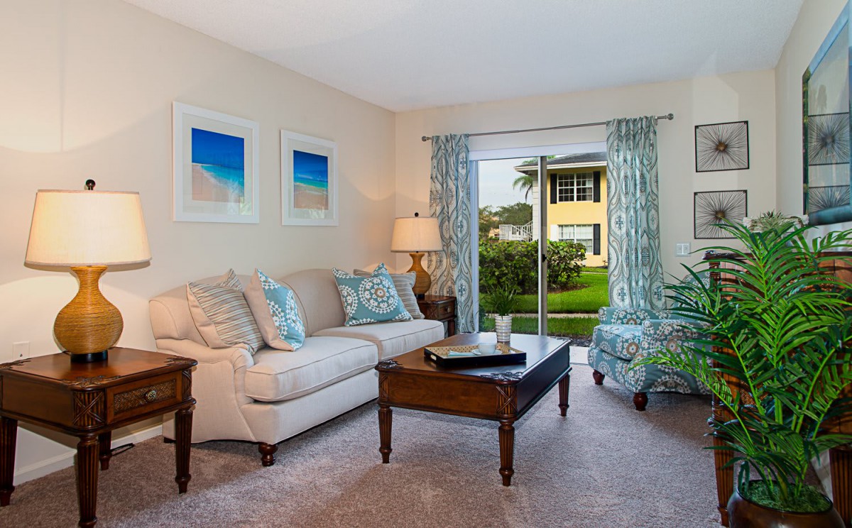 A cozy living room with a sofa, coffee table, and artwork, featuring a view of the outdoors through a sliding glass door.