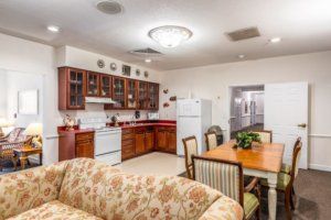 A cozy open-concept kitchen and dining area with wooden cabinets, dining table, and a floral sofa.