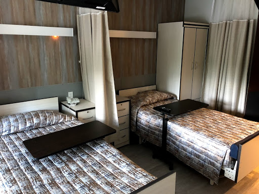 A shared hospital room featuring two beds, a wardrobe, and a television.