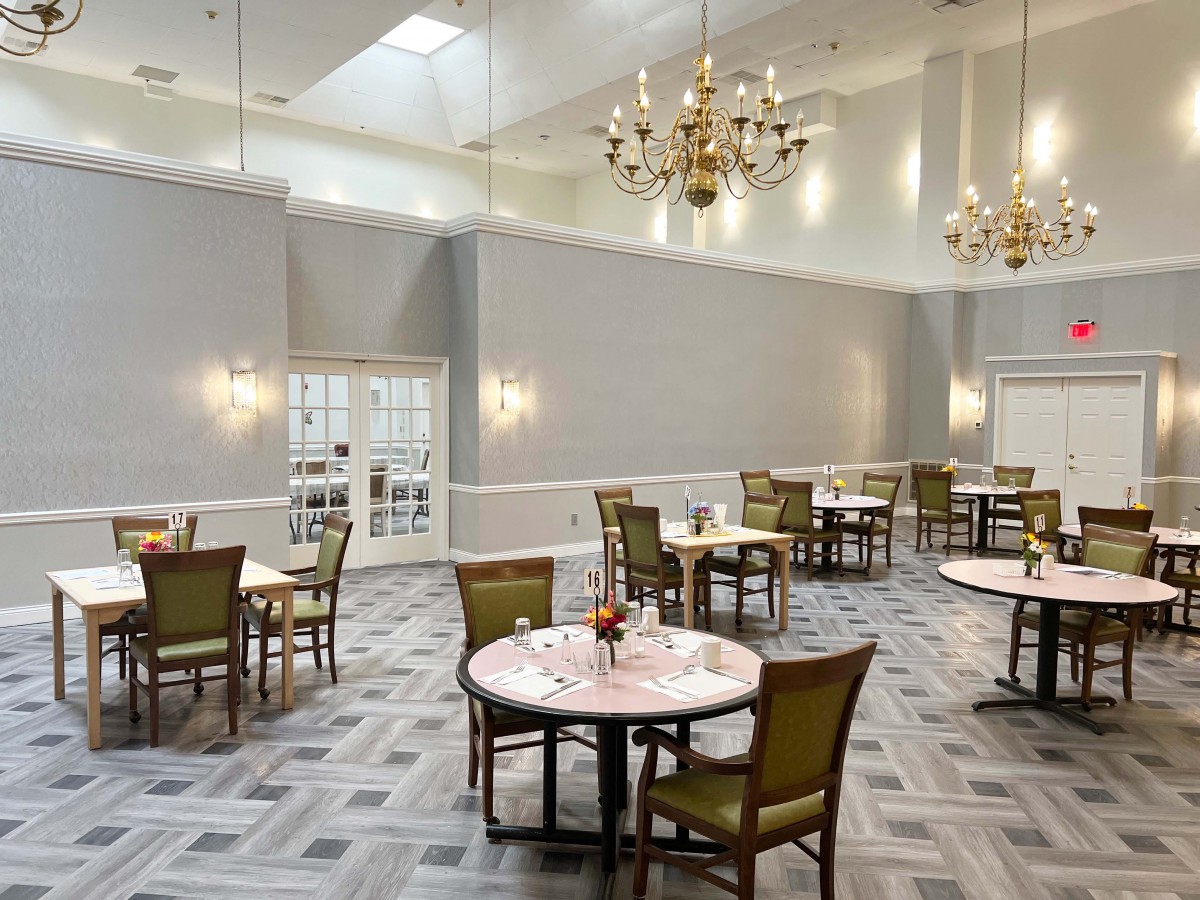 An elegant dining room with chandeliers, neatly arranged tables, and chairs on a patterned carpeted floor.