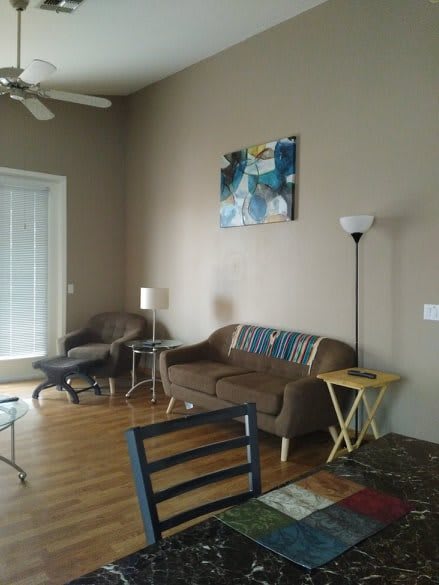 A cozy living room with a brown sofa, chairs, and a coffee table on a wooden floor, decorated with artwork on the wall.