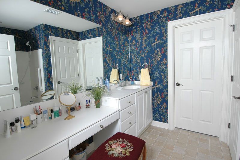 A bathroom with a floral-patterned wallpaper, a white vanity with a mirror, and various toiletries on the counter.