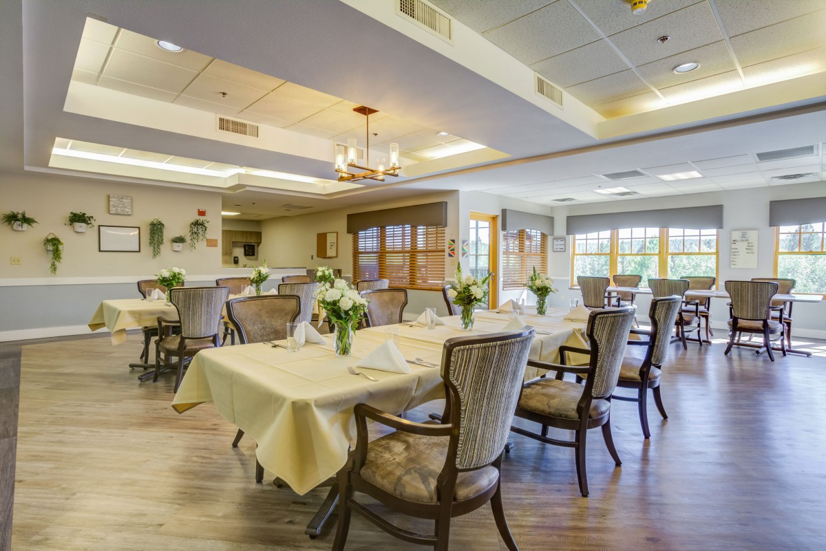 A well-lit dining room with neatly arranged tables and chairs, decorated with flowers.
