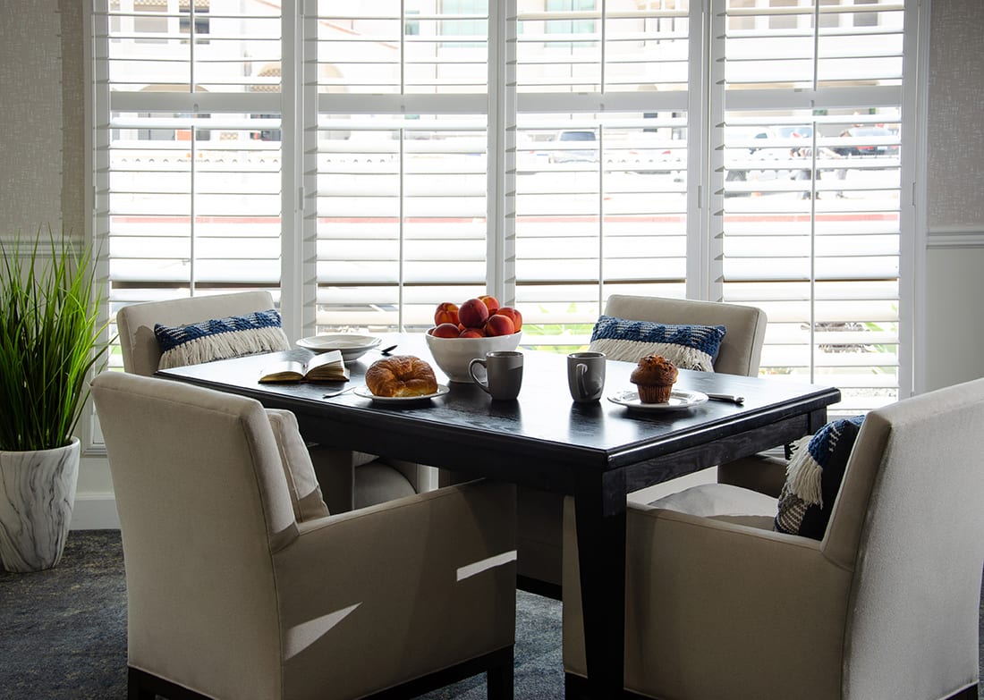 A cozy dining area with a table set for breakfast, featuring comfortable chairs and ample natural light from nearby windows.