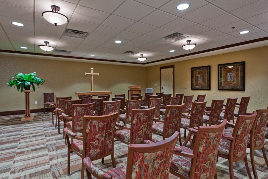 An empty chapel room with arranged chairs, a cross at the front, and warm lighting.