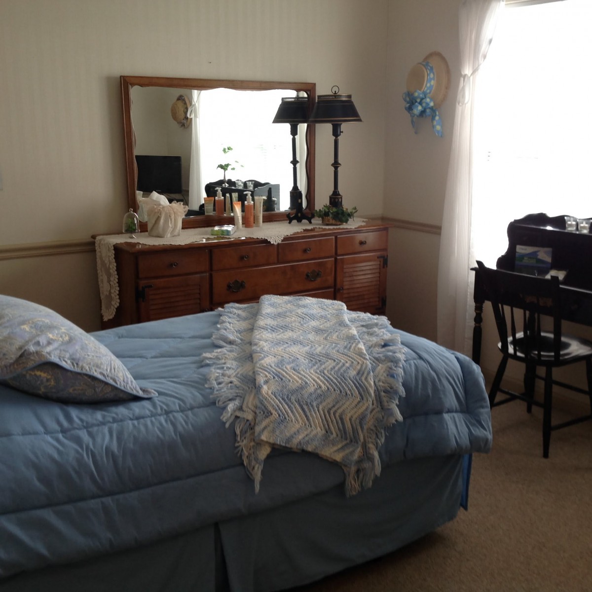 A cozy bedroom with a neatly made bed, a wooden dresser with a mirror, and a lamp on top.
