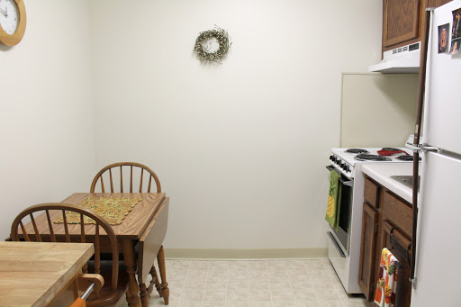 A cozy kitchen featuring a dining area with a wooden table and chairs, along with a stove and decorative wreath on the wall.