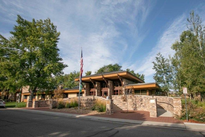 A modern house with distinct architectural design, surrounded by trees and a clear sky, featuring an American flag in front.
