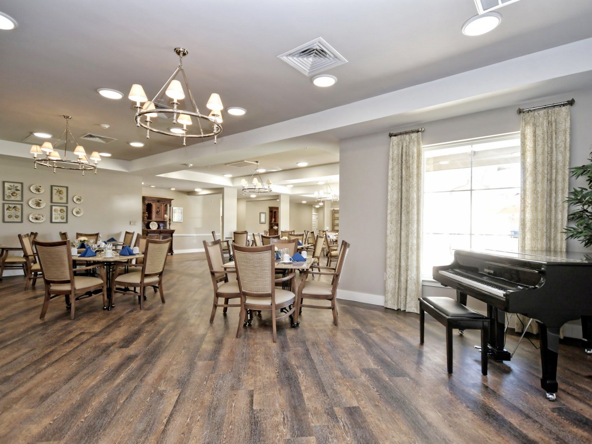 A well-lit dining area with elegant tables and chairs, featuring a piano and a chandelier.
