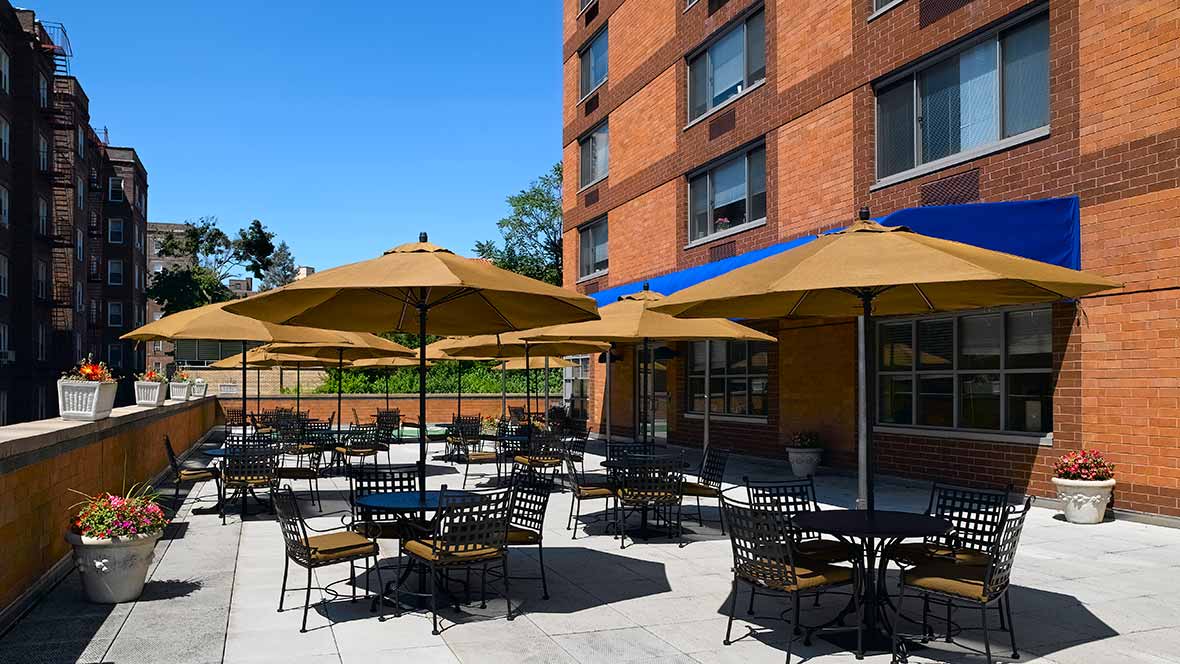 Outdoor patio area with tables and umbrellas at a building on a sunny day.