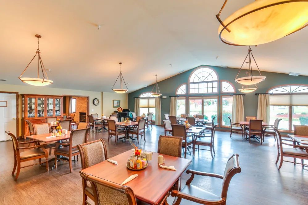 A spacious dining hall with neatly arranged tables and chairs, featuring large windows and elegant lighting.