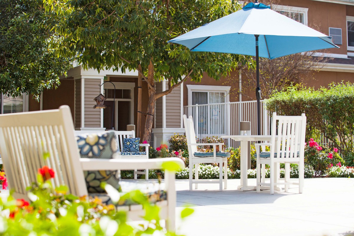 A serene patio area with outdoor furniture, a blue umbrella, and lush greenery.