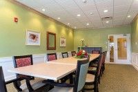A modern conference room with a long table, surrounded by chairs and adorned with green walls.