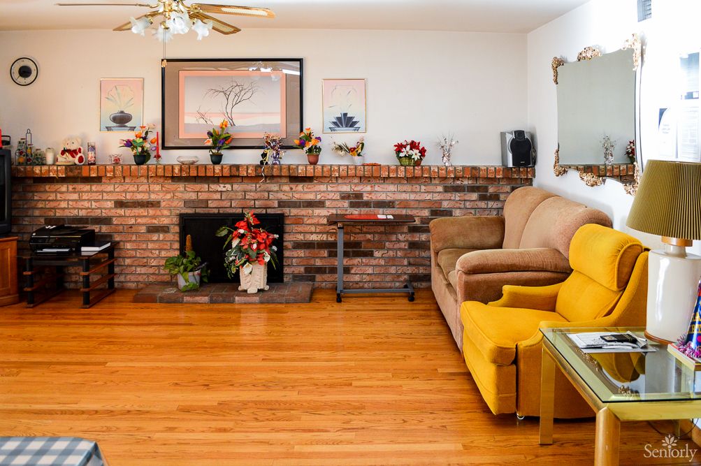 A cozy living room featuring a brick fireplace, yellow chair, and hardwood floors.
