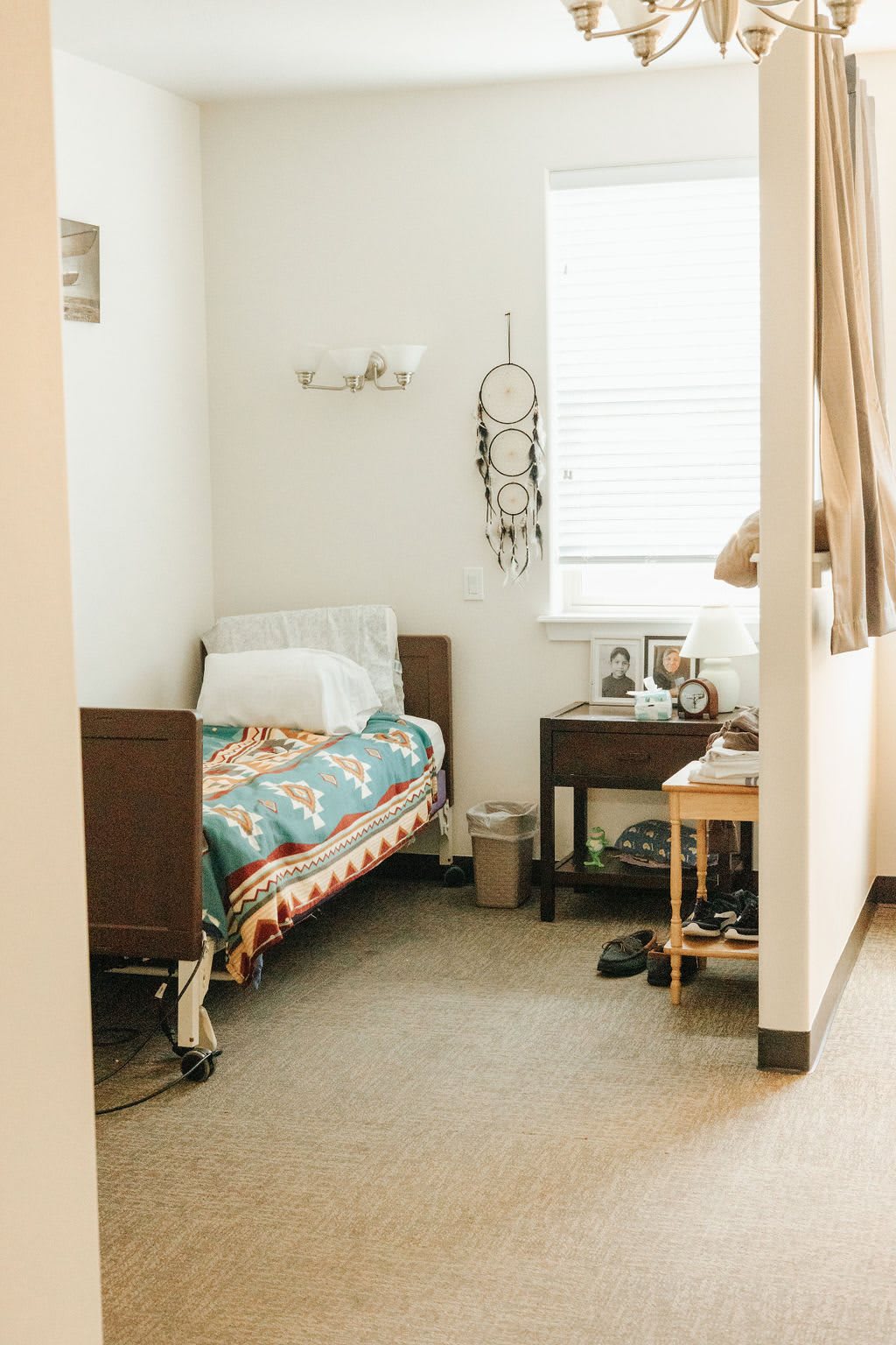 A cozy bedroom featuring a single bed with a colorful blanket, a dreamcatcher on the wall, and a nearby nightstand with a lamp.