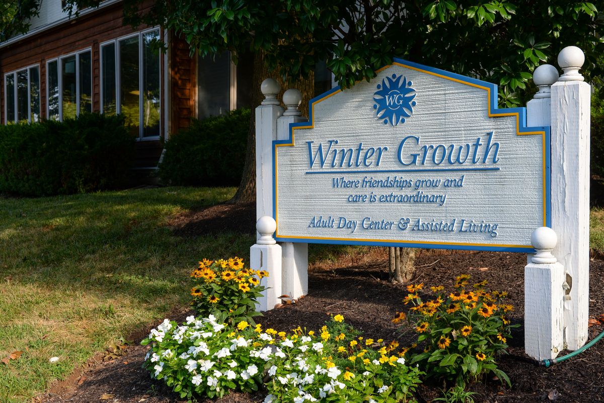 Sign outside a building surrounded by flowers and greenery.