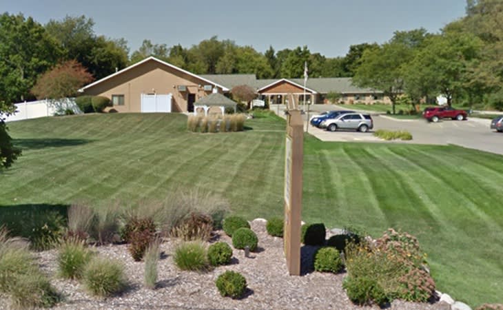 A suburban residential area with neatly mowed lawns, a driveway, and parked cars.