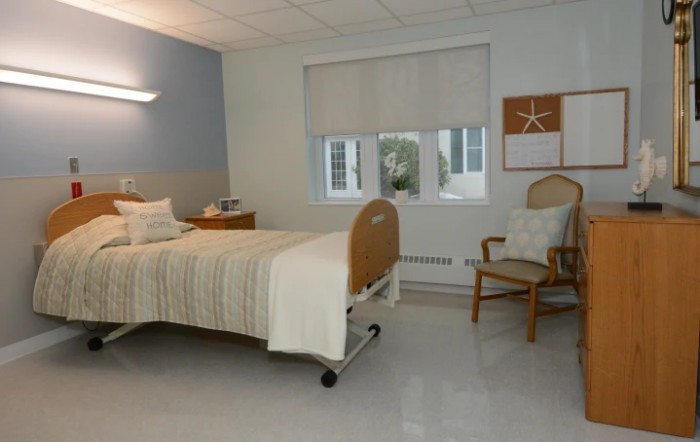 A clean and minimalist hospital room with a single bed and a chair.