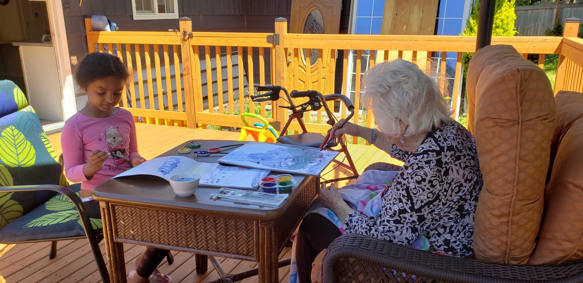 An elderly woman painting with watercolors on a sunny deck.