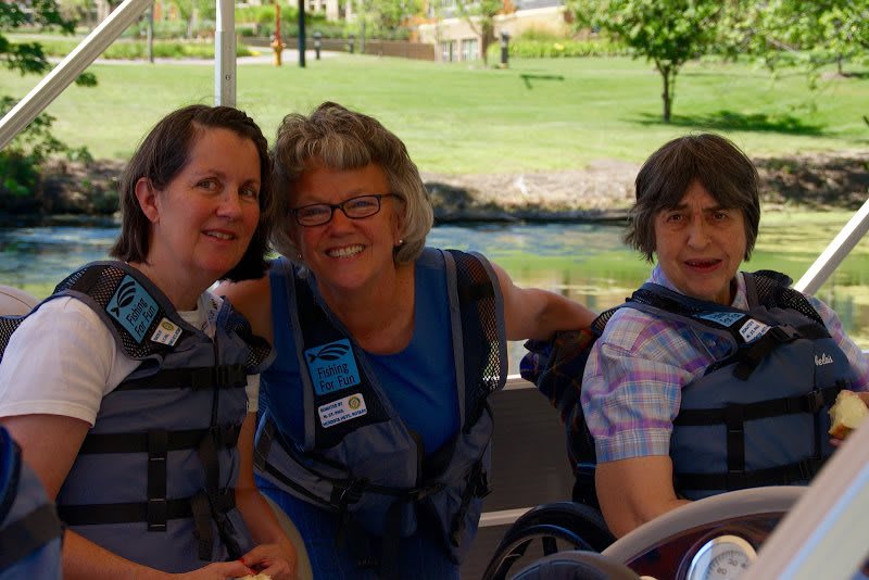A group of three people wearing life jackets, sitting outdoors and smiling.
