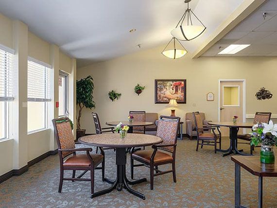A well-lit room with tables and chairs arranged for dining or meetings, featuring soft lighting and decorative wall elements.