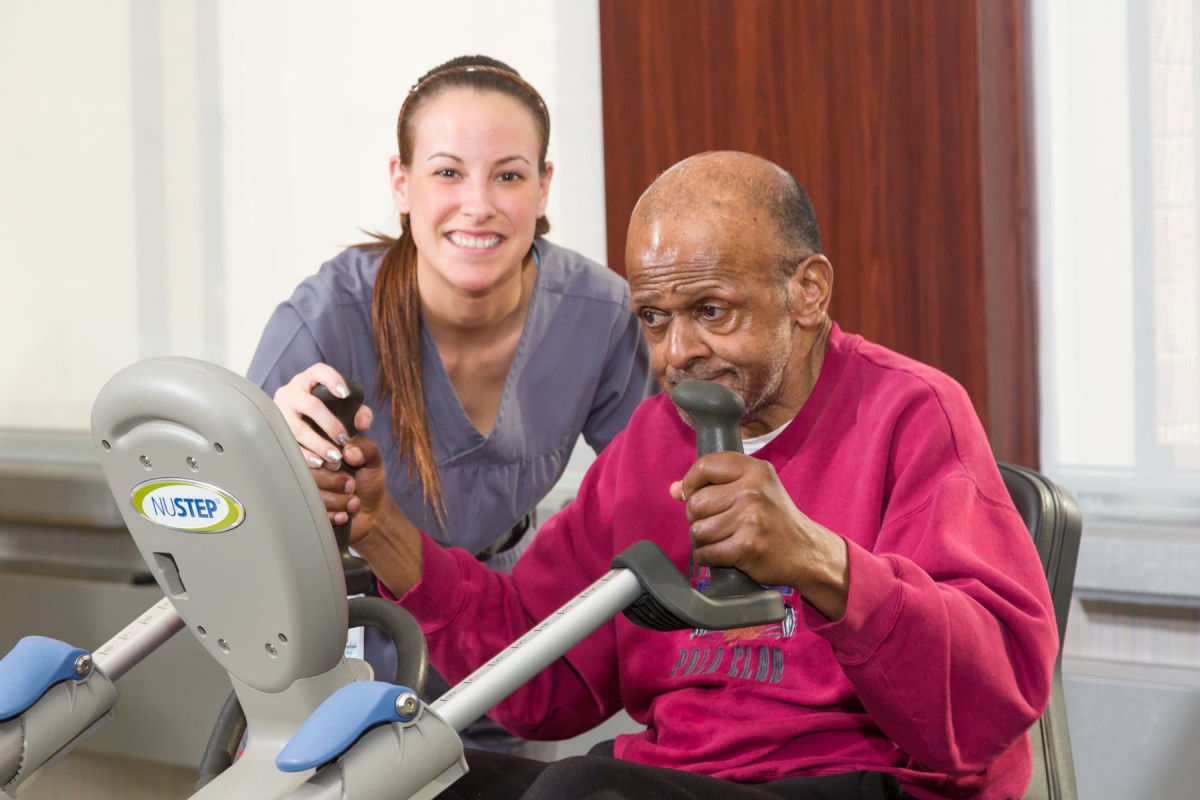 An elderly man exercising with the assistance of a healthcare worker.