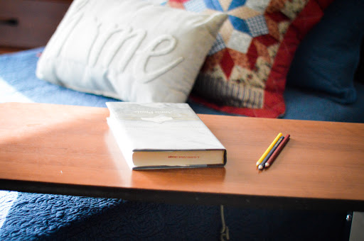 A cozy reading spot featuring a book, a decorative pillow, and a yellow pencil on a wooden table.