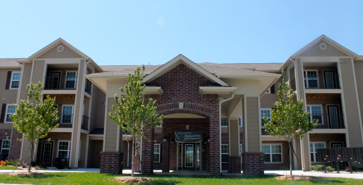 A modern apartment building with a central entrance and landscaped surroundings.
