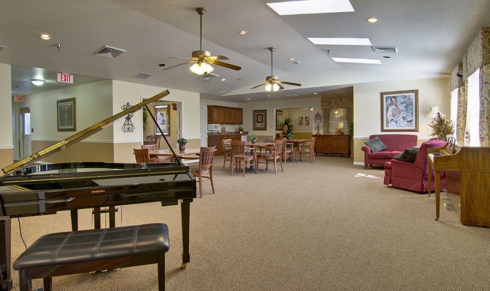A spacious room featuring a grand piano, ceiling fans, and a seating area with tables and chairs.