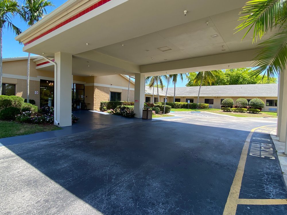 An outdoor view of a building entrance with an awning and surrounding palm trees.