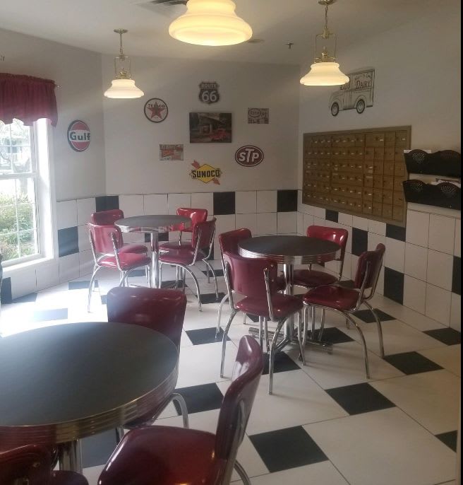 A retro-style diner with red chairs, round tables, and a checkerboard floor.