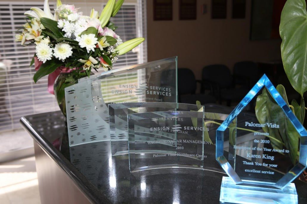 A collection of glass awards displayed on a table with flowers in the background.