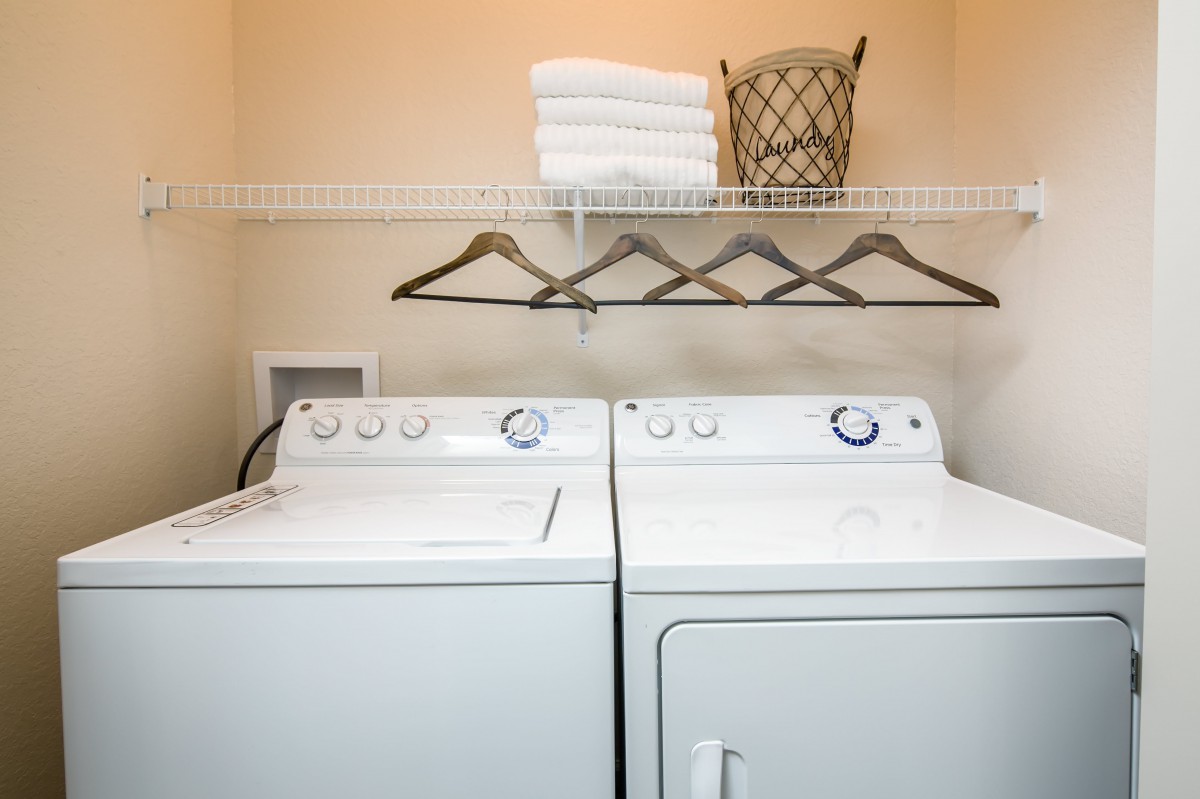 A laundry room featuring a washing machine and dryer underneath a shelf with neatly folded towels, hangers, and a wicker basket.