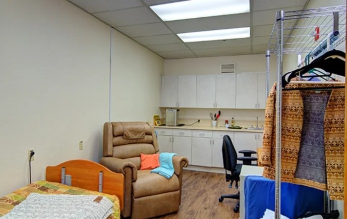 A clinic treatment room with a recliner chair, desk, and cabinets.