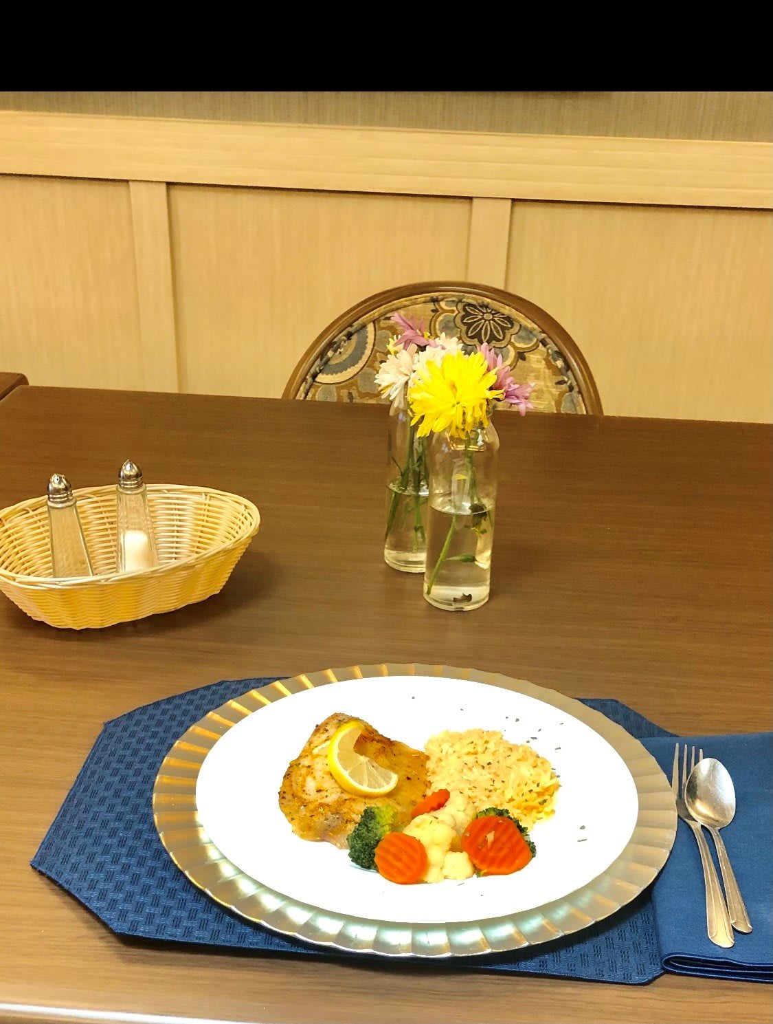 A beautifully set dining table with a plated meal and a vase of flowers.