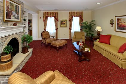 A traditionally styled living room with rich red carpeting, cushioned furniture, and elegant drapery.