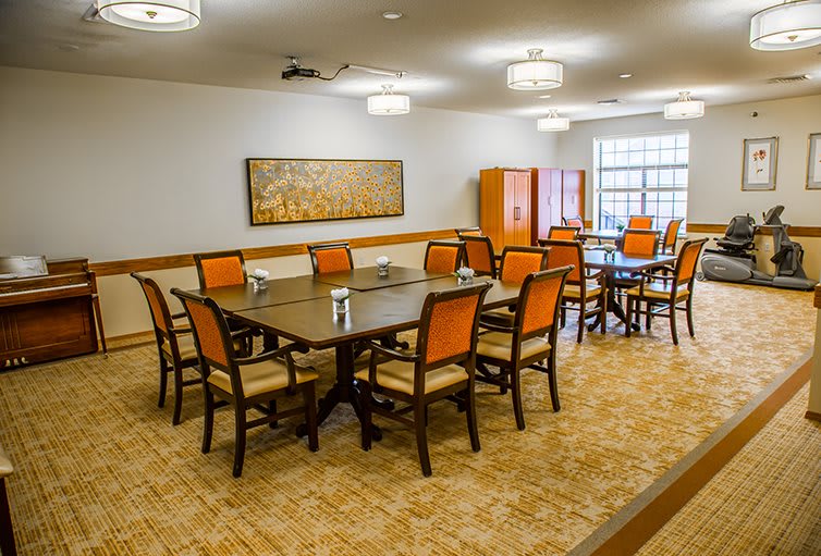 A well-lit dining room with a large table and multiple chairs arranged around it.