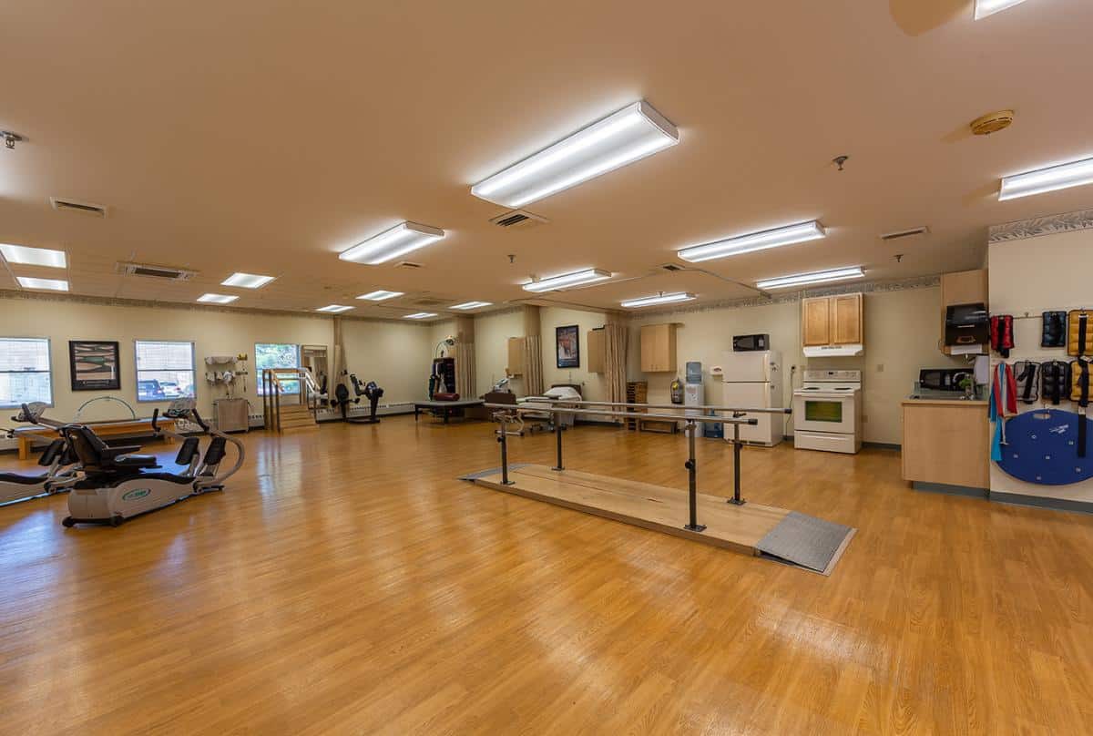 A spacious rehabilitation room equipped with exercise equipment and parallel bars for physical therapy.